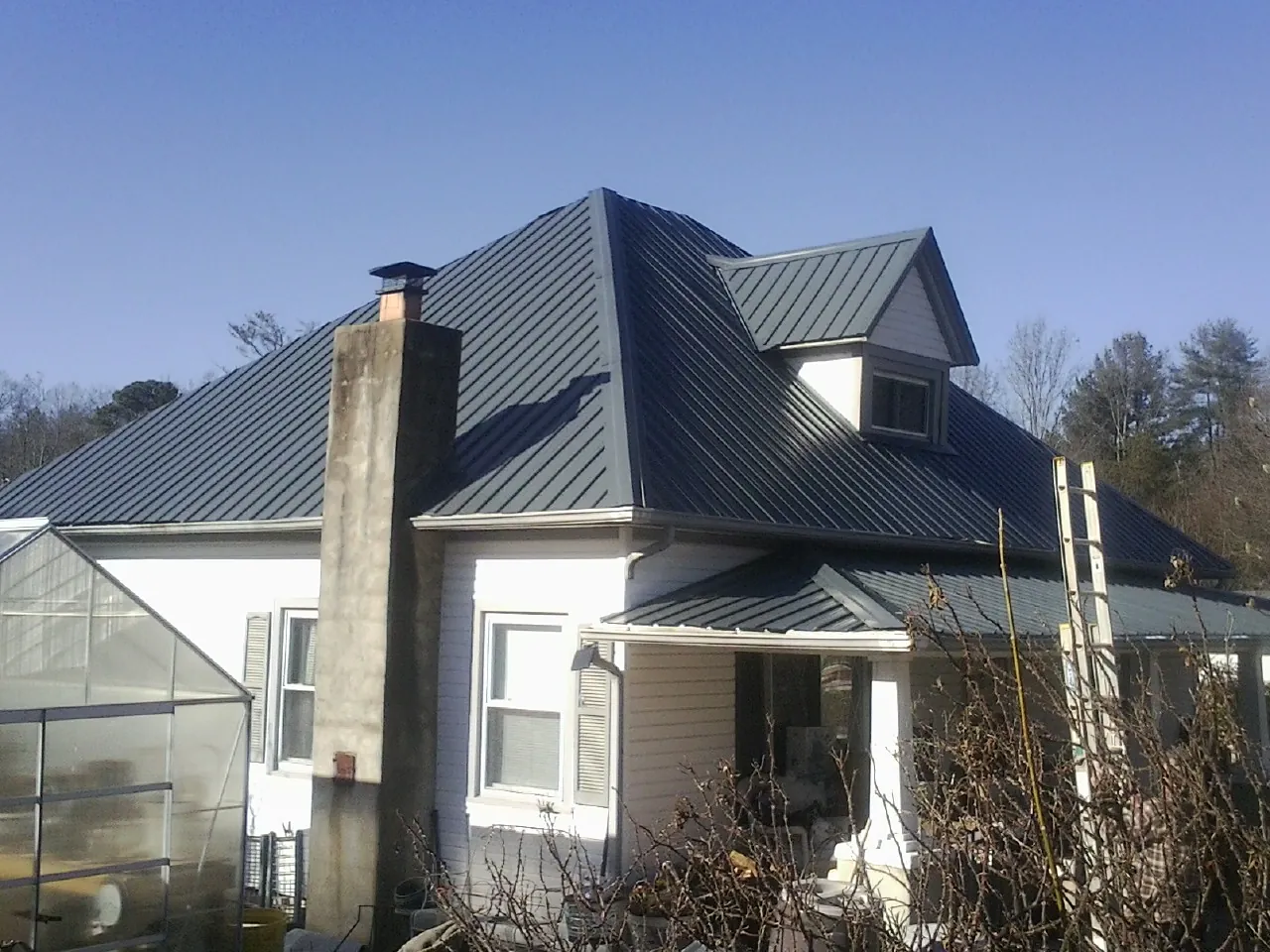 Dark blue standing seam metal roof on a white farmhouse with dormer — Slate & Tile Roof Repair by Roofing Brothers in Powers Lake