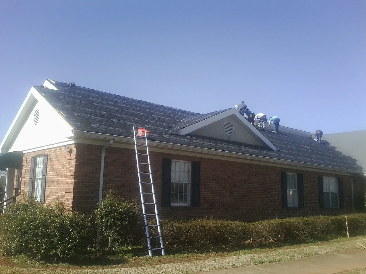 Crew tearing shingles off a brick ranch roof with a ladder set — Emergency Roof Repair work by our crew in Powers Lake