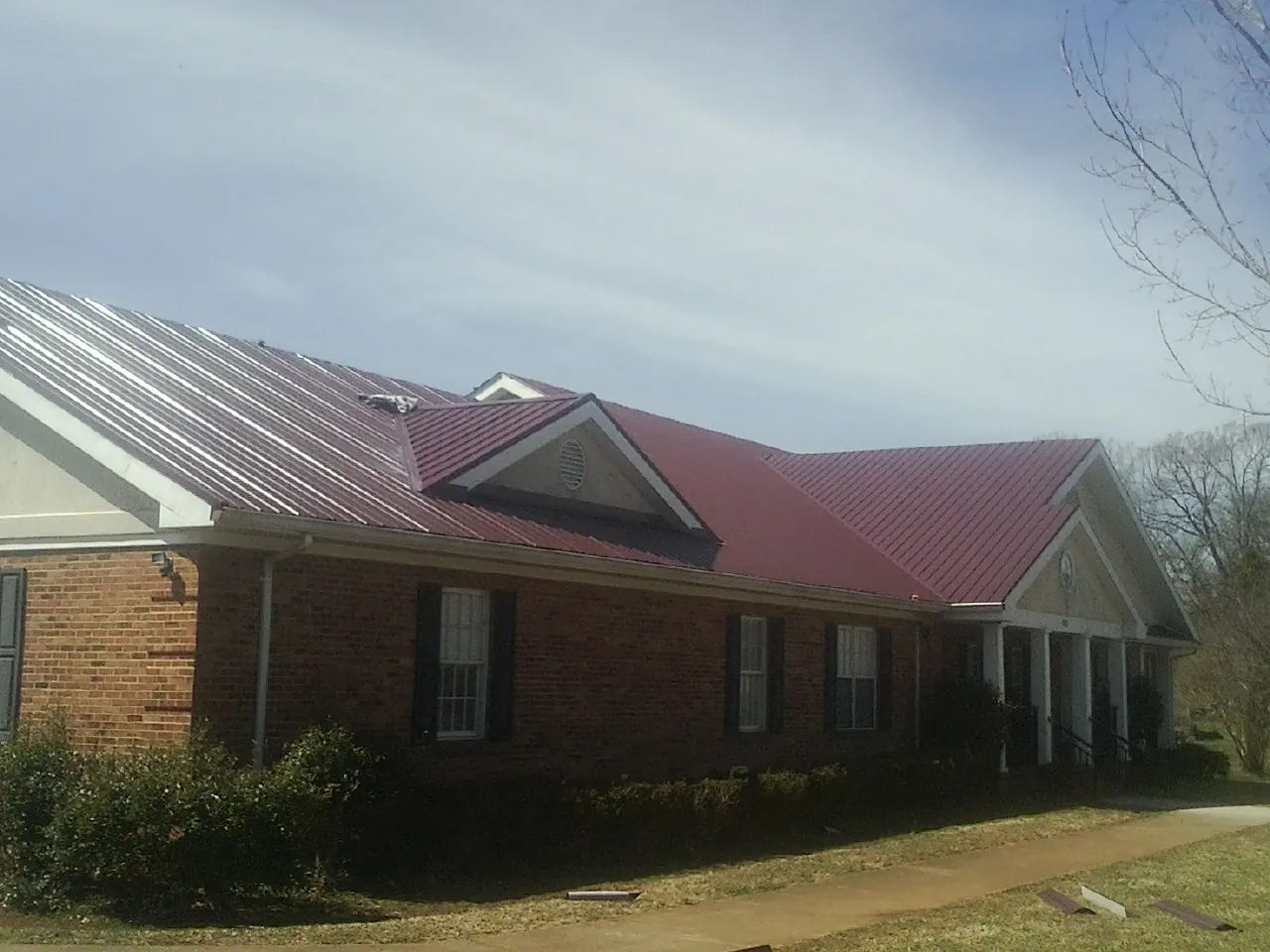 Red metal roof with gabled entries on a long brick building, from a Hail Damage Roof Repair job in Powers Lake