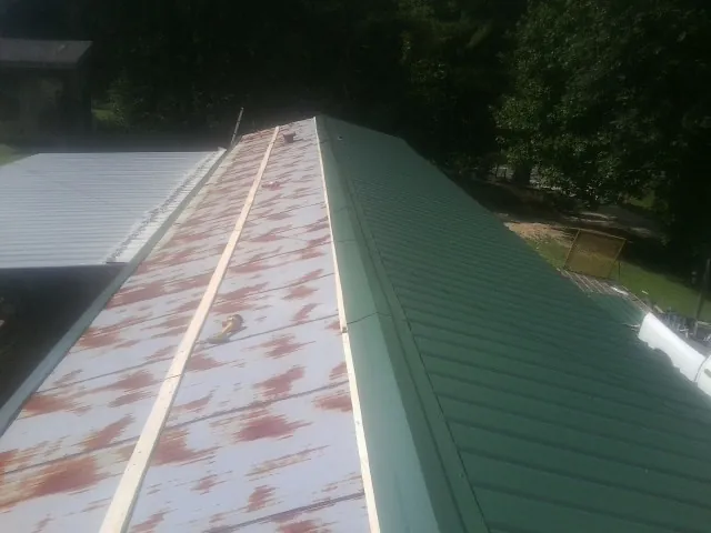 Old rusted panels beside newly installed green metal roofing — Wind Damage Roof Repair by Roofing Brothers in Powers Lake