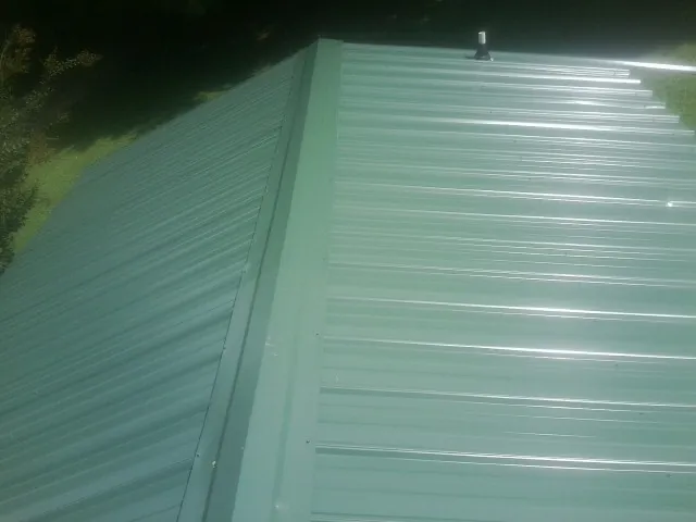 New green metal panels meeting at the ridge of a roof — Flat Roof Repair work by our crew in Powers Lake