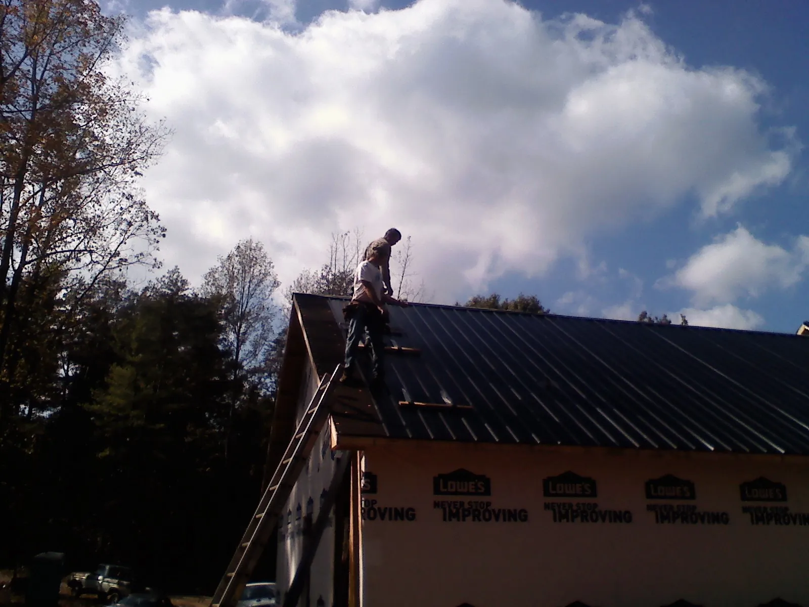 Roofer fastening dark metal panels high against a cloudy sky, from a Roof Inspection job in Powers Lake