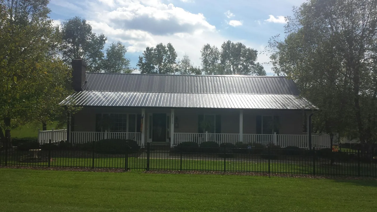 Gray metal roof on a brick ranch with a full width front porch — Gutter Guard Installation work by our crew in Powers Lake