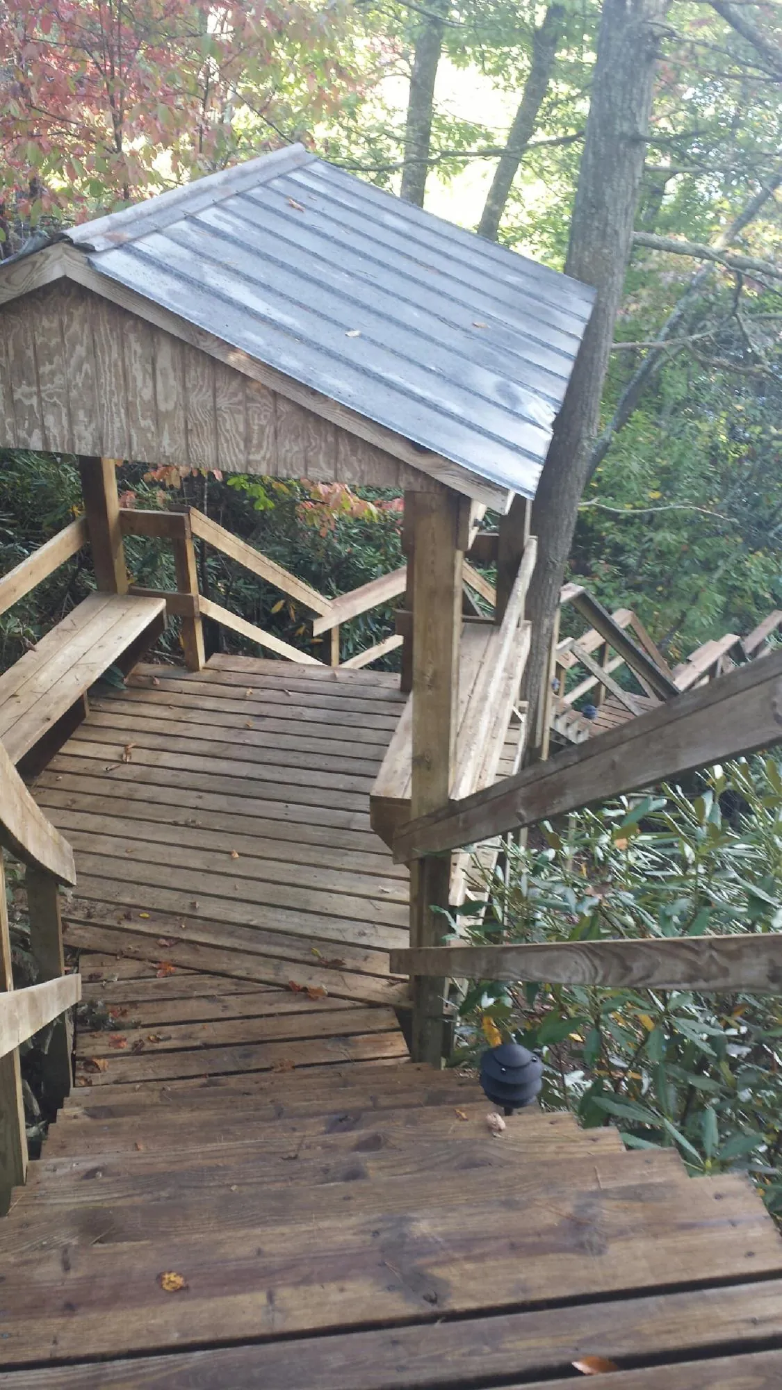 Metal roofed shelter over wooden steps on a wooded walkway — Skylight Repair & Installation work by our crew in Powers Lake