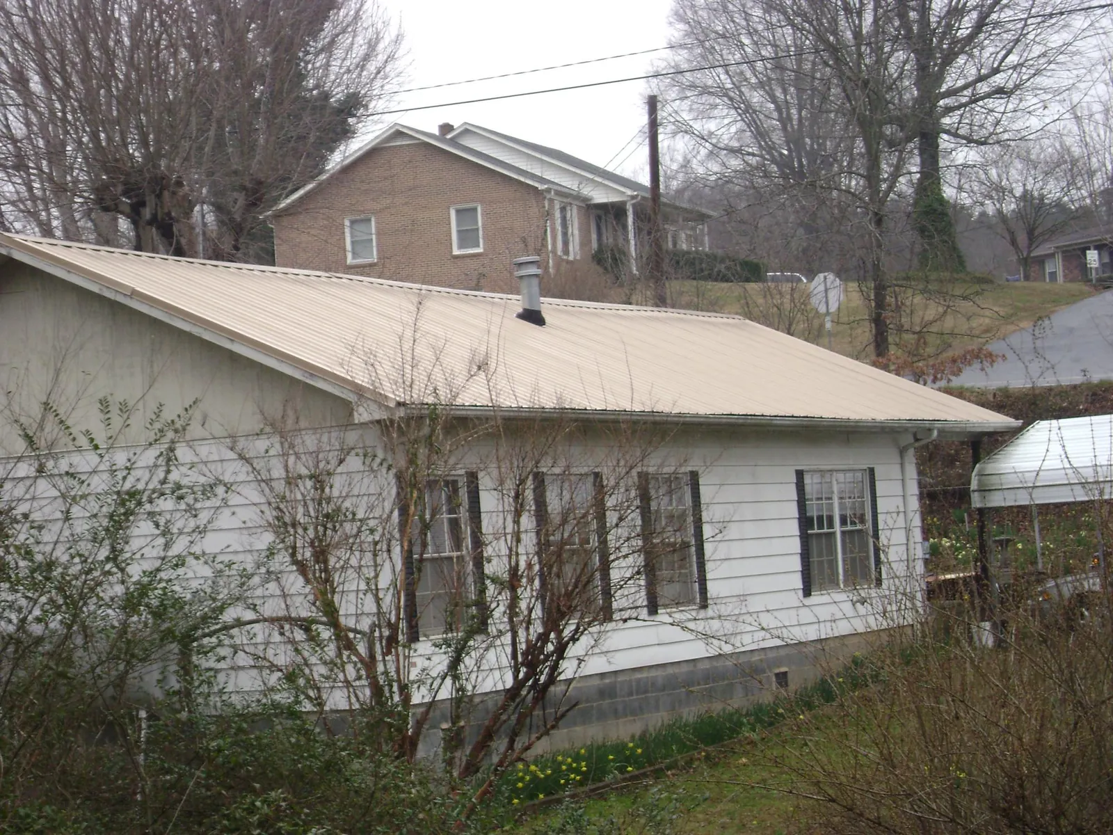 Tan metal roof on a white sided house set into a hillside — Commercial Roofing by Roofing Brothers in Powers Lake