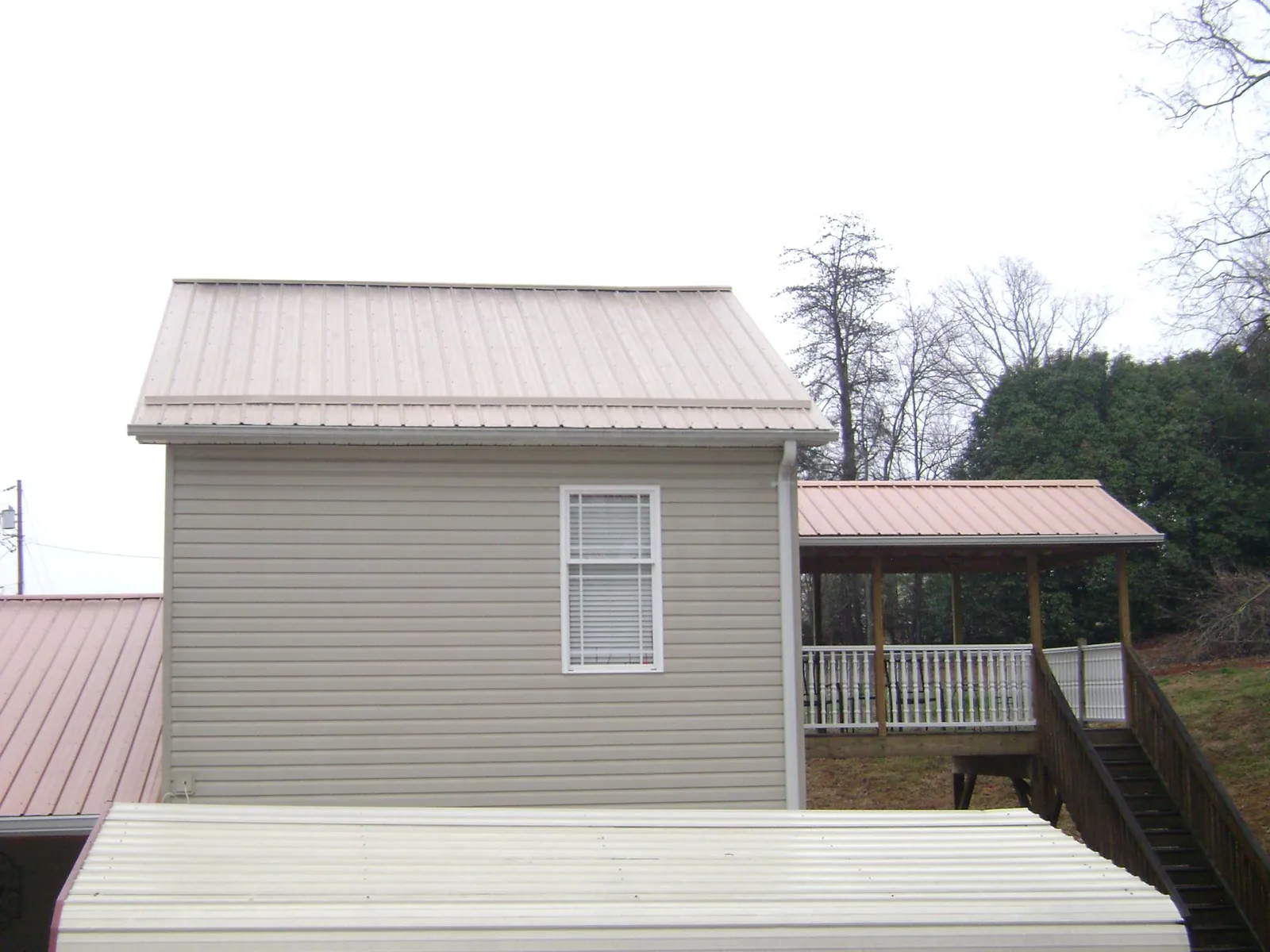 Tan metal roofs on a two story addition and attached porch, from a Roof Replacement job in Powers Lake