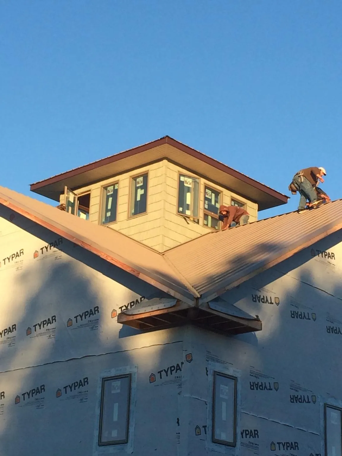 Roofers working around a rooftop cupola on a new metal roof at sunset — Roof Waterproofing in Powers Lake by Roofing Brothers